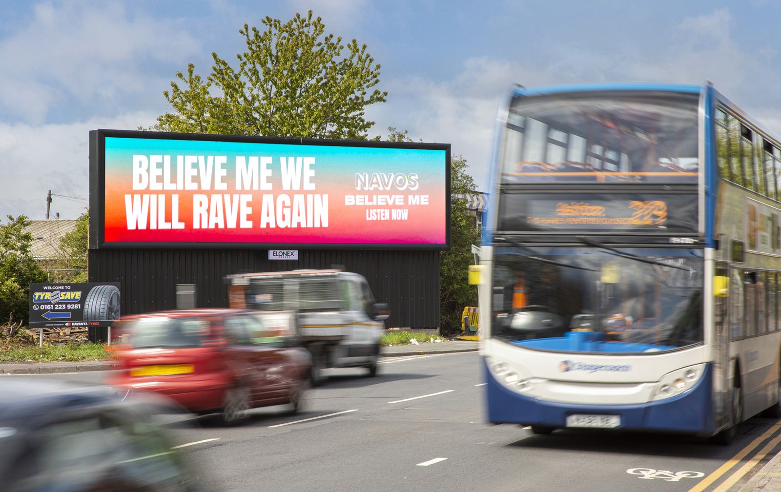 A wide digital roadside billboard on a busy road with a bus passing