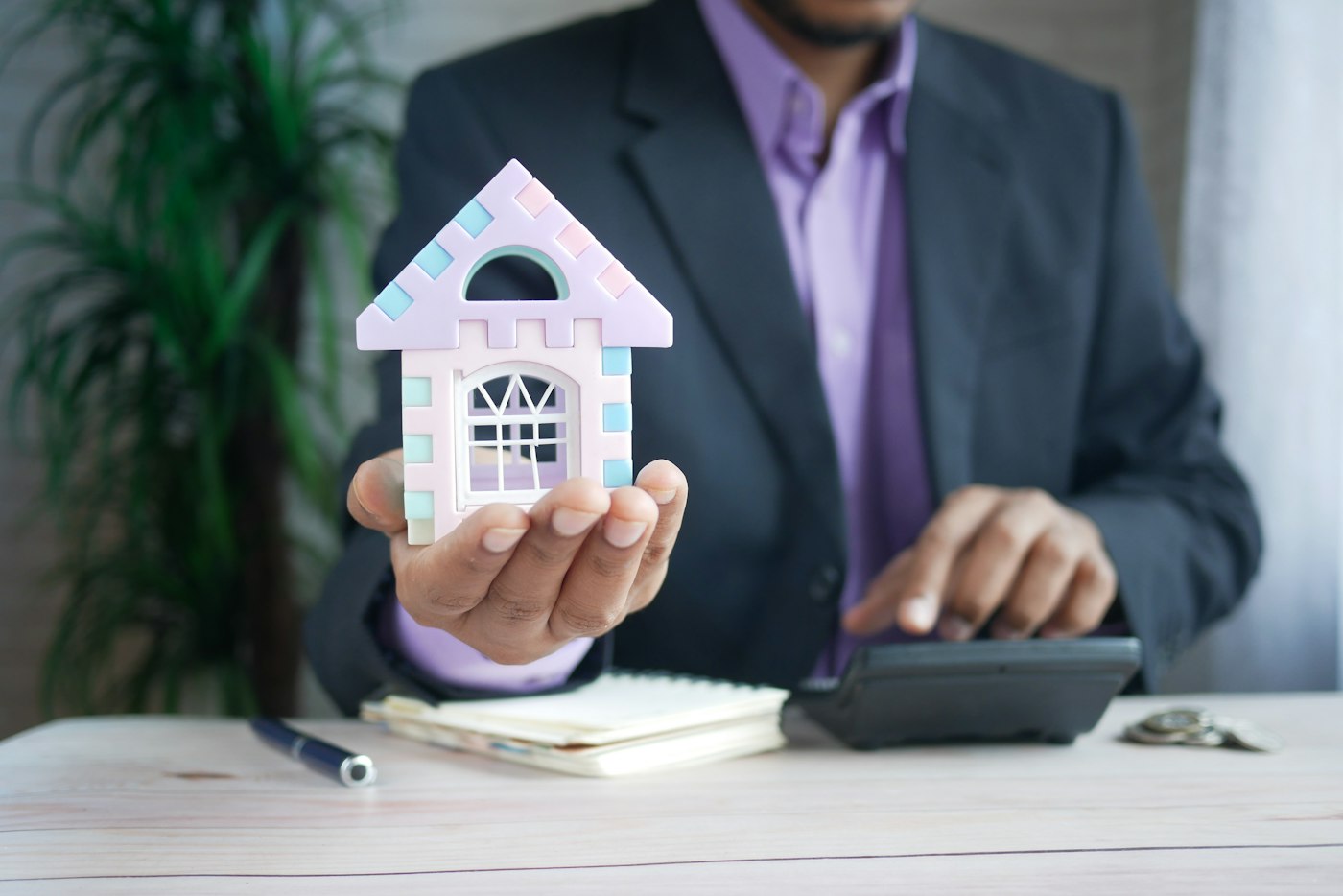 An estate agent holding a small model house at his desk