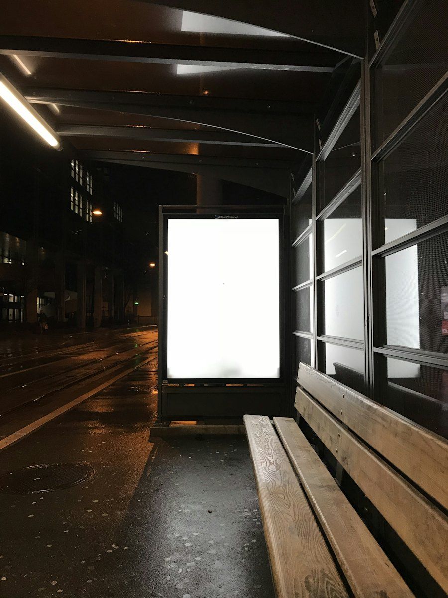A glowing advertising screen at a bus stop at night